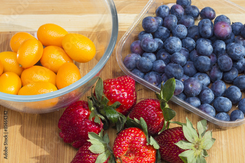 kumquat  strawberries and blueberries on a cutting board