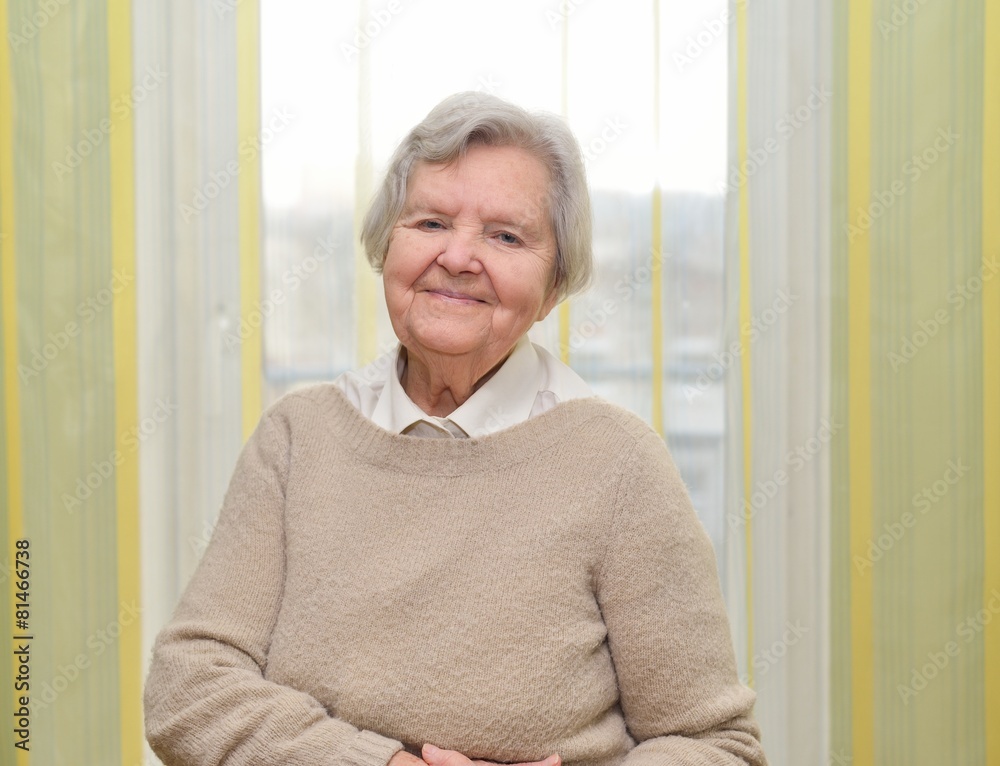 Senior happy woman in her home with window on background.
