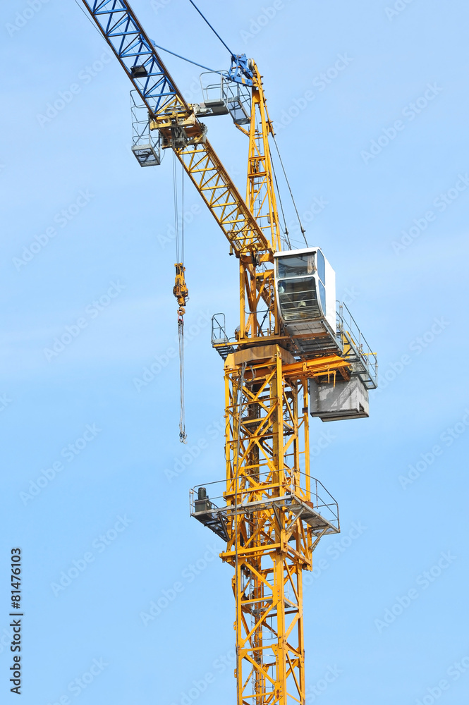 Yellow construction tower crane against blue sky Yellow construction tower crane against blue sky