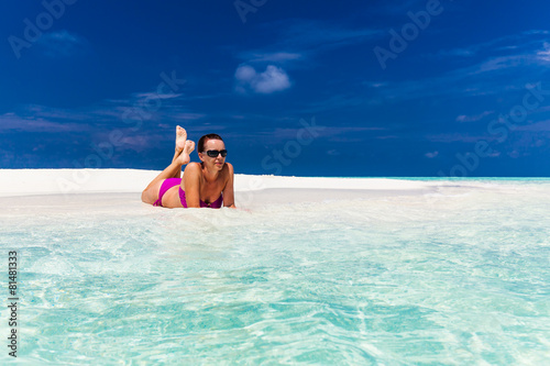 Young woman in purple bikini relaxing on sand on tropical beach