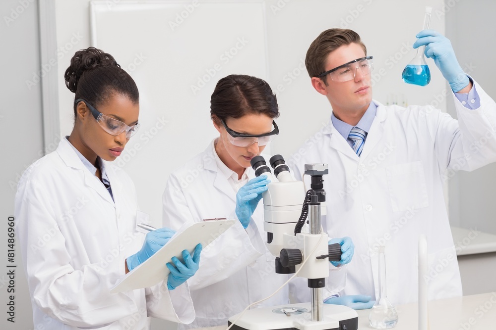 Scientists working attentively with microscope and beaker Scientists working attentively with microscope and beaker