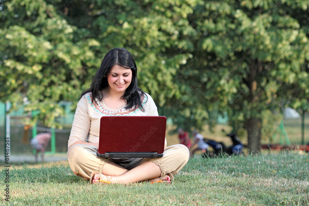 Obraz premium happy girl with laptop sitting on grass in park