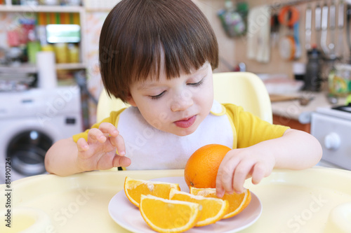 Lovely little child eating orange