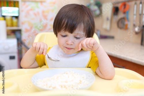 thoughtful little boy eating quark with sour cream on kitchen