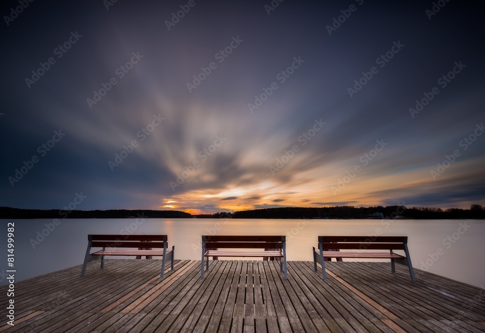 Beautiful long exposure lake with pier on foreground and bench.