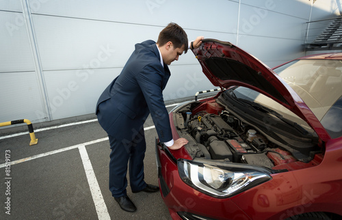 Stressed businessman looking under the car hood