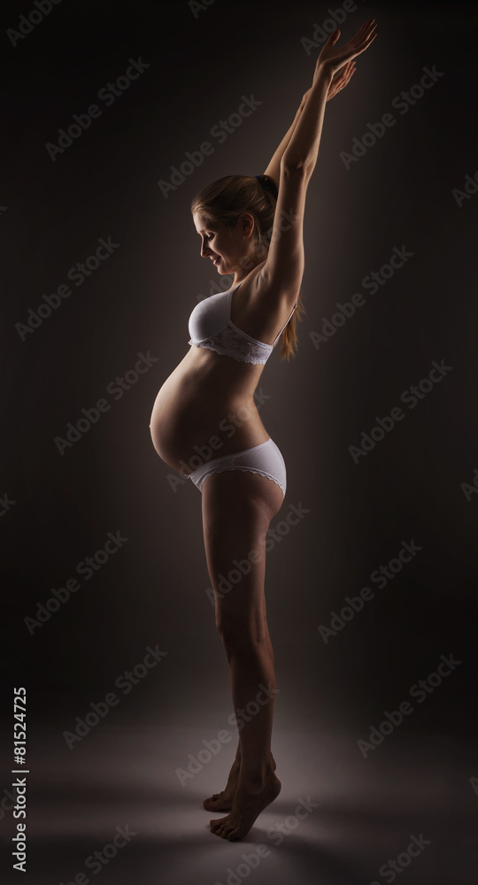 Young pregnant woman stretching up and looking at her belly