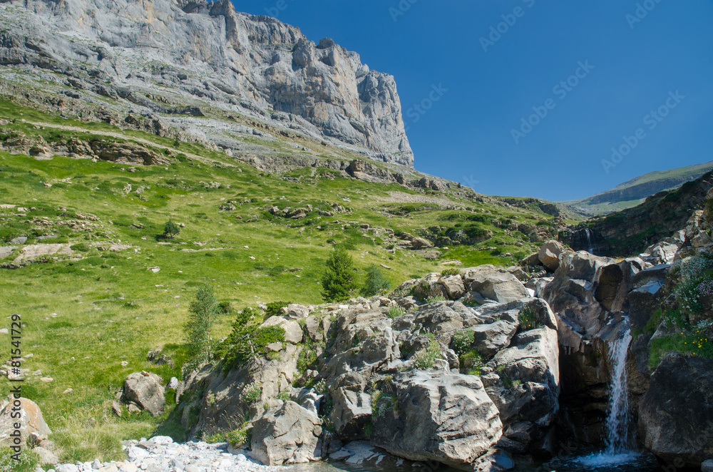 Pyrenees waterfall in mountain forest under blue sky.
