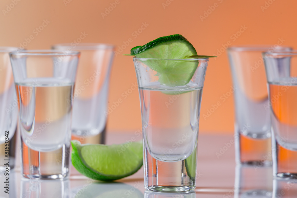 Tequila shot with a slice of lime on the glass orange background Tequila shot with a slice of lime on the glass orange background