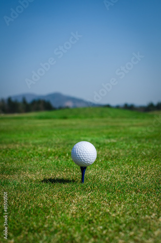 Golf ball on teeing area with green grass ahead and mountains in