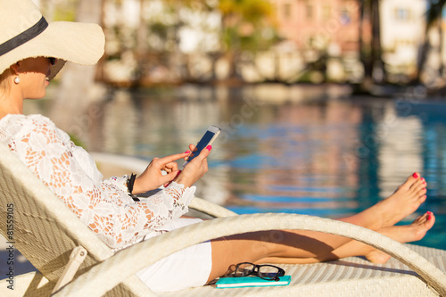 Woman sitting in chair by the swimming pool and using smartphone