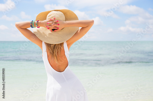 Young woman in white dress and summer hat on the beach