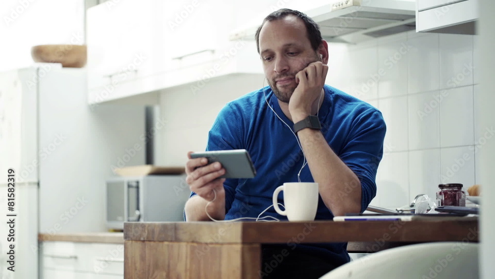 Man watching movie on smartphone and drinking coffee by table Man watching movie on smartphone and drinking coffee by table