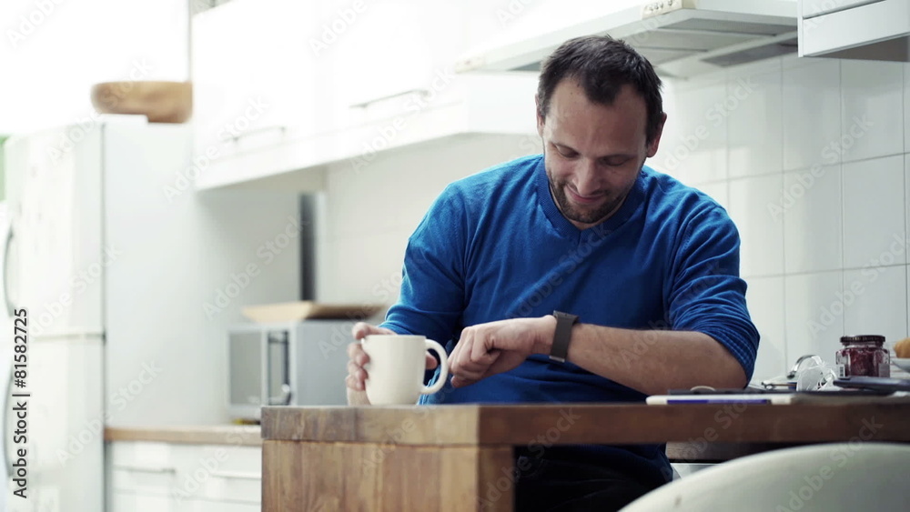 Handsome man with smartwatch drinking coffee by table in kitchen Handsome man with smartwatch drinking coffee by table in kitchen