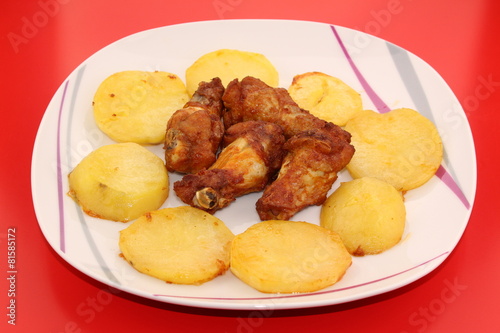 Baked and sauced chicken drumsticks surrounded by potatoes