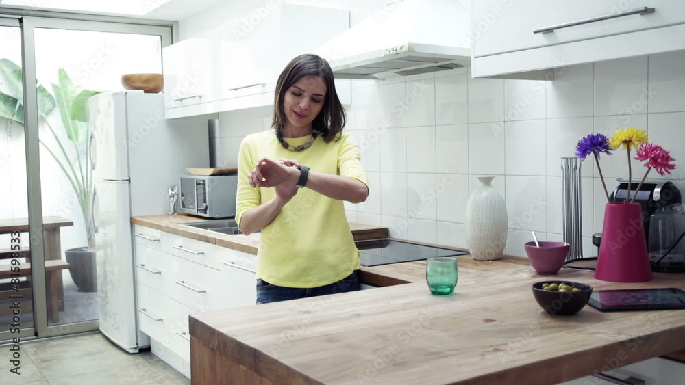 pretty woman with smartwatch standing by table in kitchen