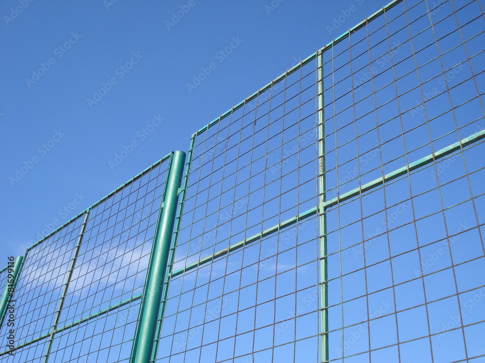Part of metal grid tall fence, against blue sky Part of metal grid tall fence, against blue sky