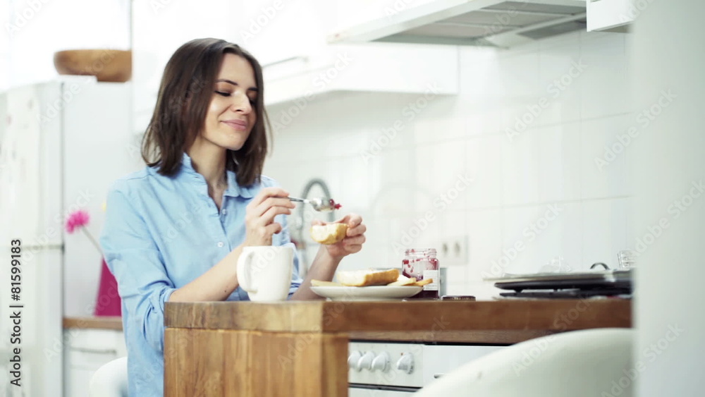 Young woman preparing sandwich, eating and drinking coffee by ta Young woman preparing sandwich, eating and drinking coffee by ta