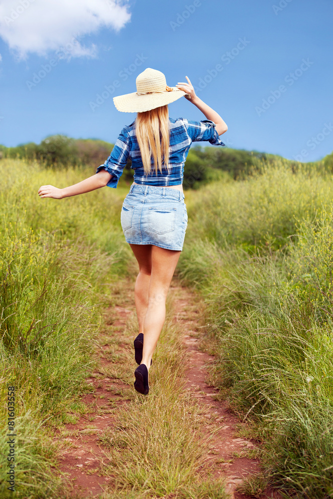 back of female model skipping in a field during summer time 