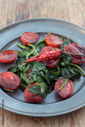 Fried tomatoes with spinach leaves and chili.