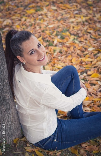 Portrait of a young attractive woman sitting in the park. Autumn leaves and colors.