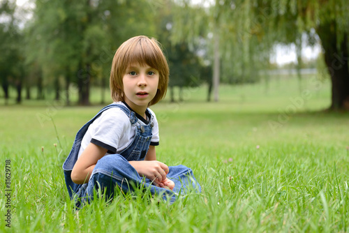 Cute little boy sitting in green grass, summer nature outdoor © Khorzhevska
