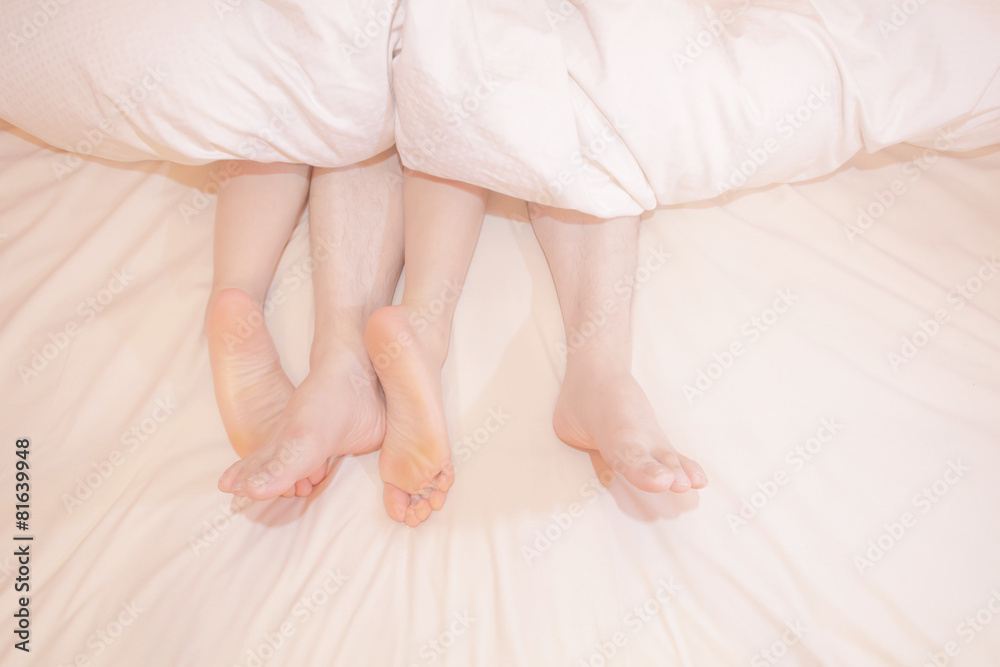 Two pairs of feet under the covers at home in bedroom Two pairs of feet under the covers at home in bedroom
