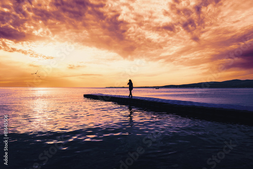 Woman walking on pier at sunset