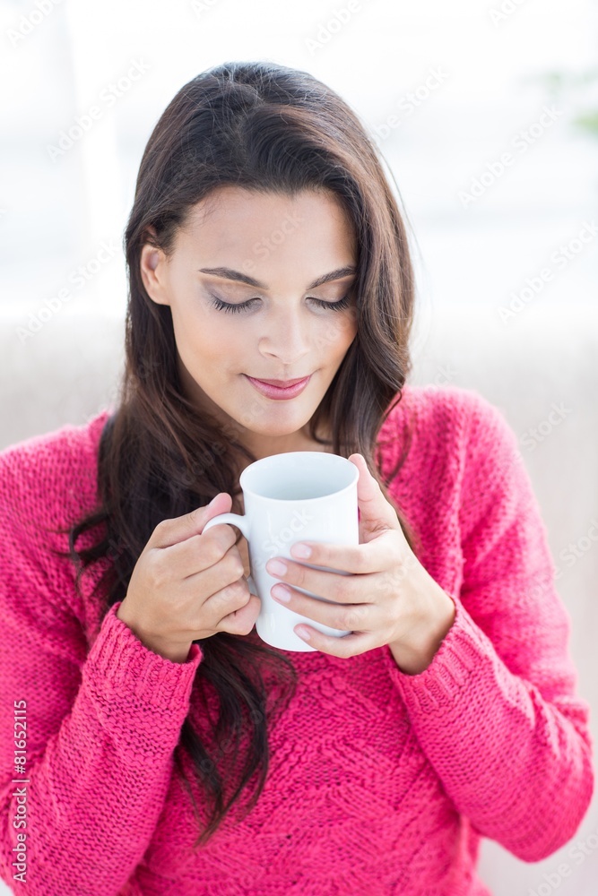 Smiling beautiful brunette relaxing on the couch and holding mug Smiling beautiful brunette relaxing on the couch and holding mug
