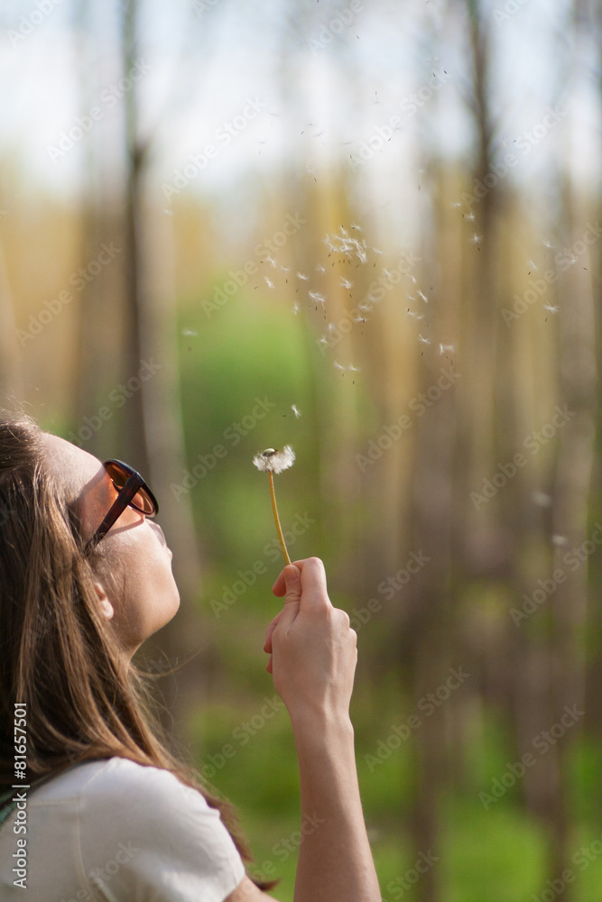 Young woman in the park holding blowing dandelion seed