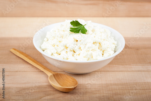 Fresh cottage cheese in a white bowl with spoon on a wooden.
