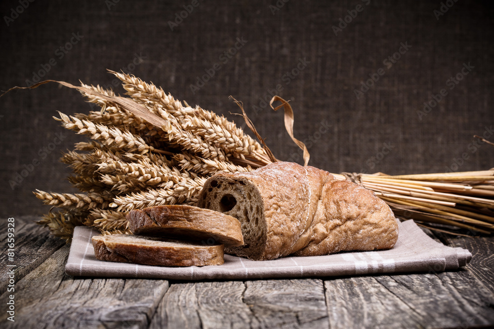 Tasty bread with wheat on wooden background.