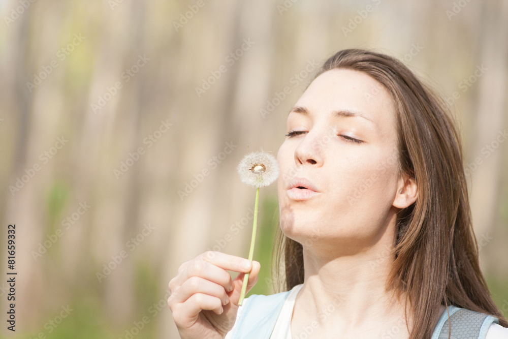 Young woman in the park holding blowing dandelion flower seed