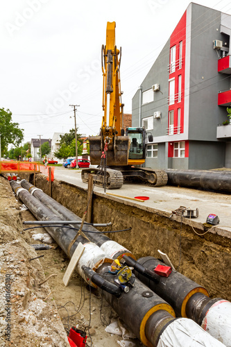 Canvas Print Yellow excavator at construction site in urban settlement