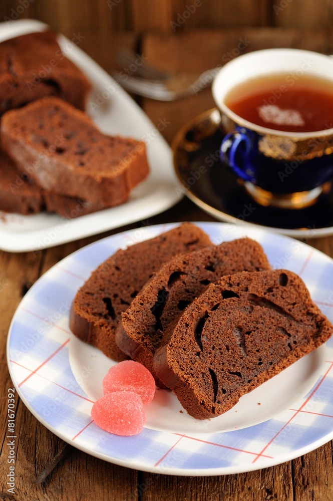 Homemade chocolate cake cut with pink candies and tea in blue cu Homemade chocolate cake cut with pink candies and tea in blue cu