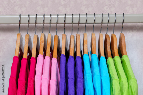 Multicolored women's t-shirts hanging on wooden hangers.