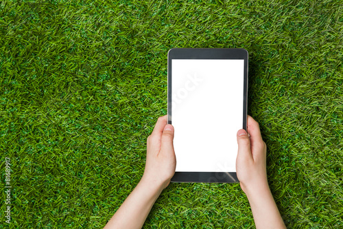 Child hand holding tablet pc. over green grass