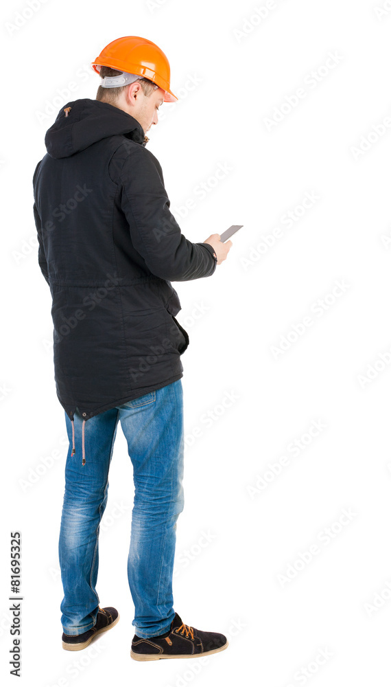 Backview of an engineer in construction helmet stands and using Backview of an engineer in construction helmet stands and using