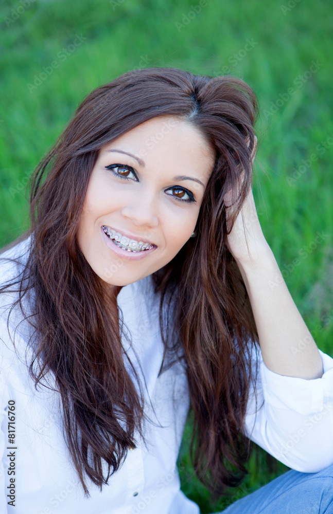 Brunette girl with brackets sitting on the grass Brunette girl with brackets sitting on the grass