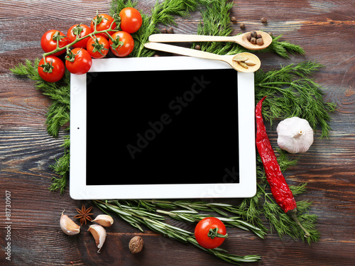Digital tablet with fresh herbs, tomatoes and spices