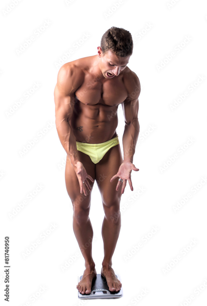 Unhappy muscular young man weighing himself on scale, isolated Unhappy muscular young man weighing himself on scale, isolated