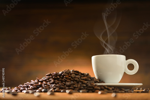 Cup of coffee with smoke and coffee beans on  wooden background