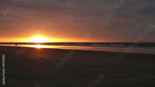 a man walking in the distance along the beach at sunrise