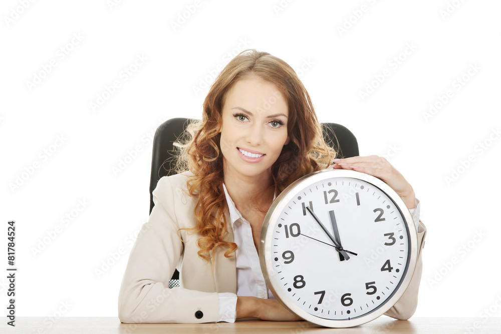 Businesswoman with clock by a desk.