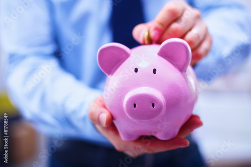 Businessman putting money into a piggy bank isolated on white