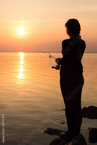 silhouette of a girl on the bank of the river with a fishing rod