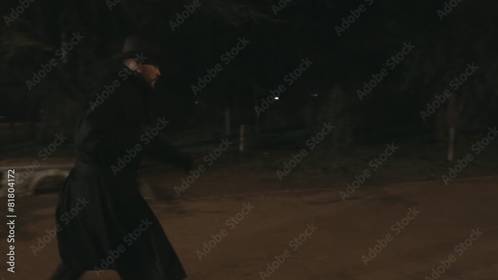 Man in a black cloak and hat runs through the park at night for Man in a black cloak and hat runs through the park at night for