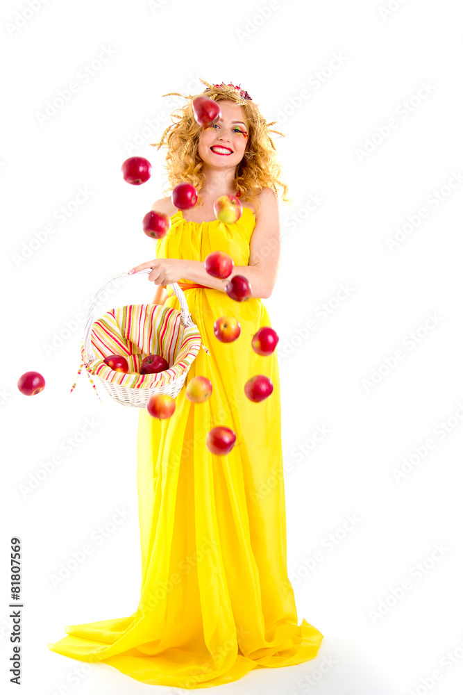 The beautiful girl dressed in yellow is throwing red apples