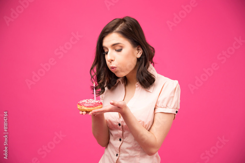 Woman holding donut and blowing on candle