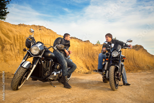 Two bikers on unknown motocycles talking on desert road